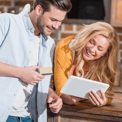happy beautiful couple making e-shopping with tablet on table at kitchen